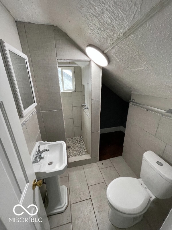 bathroom with tile flooring, a textured ceiling, vaulted ceiling, tile walls, and toilet