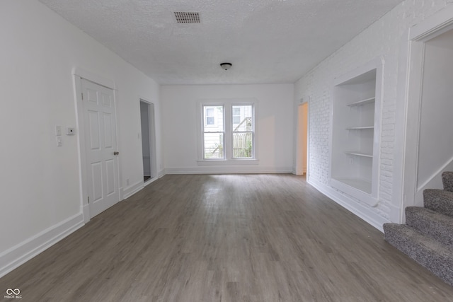 unfurnished living room with built in features, dark hardwood / wood-style flooring, and a textured ceiling