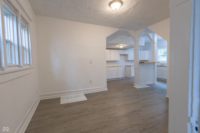 unfurnished living room featuring decorative columns, dark hardwood / wood-style floors, and a textured ceiling