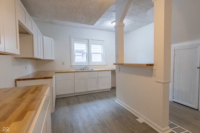 kitchen featuring white cabinetry, wood-type flooring, sink, butcher block countertops, and a textured ceiling