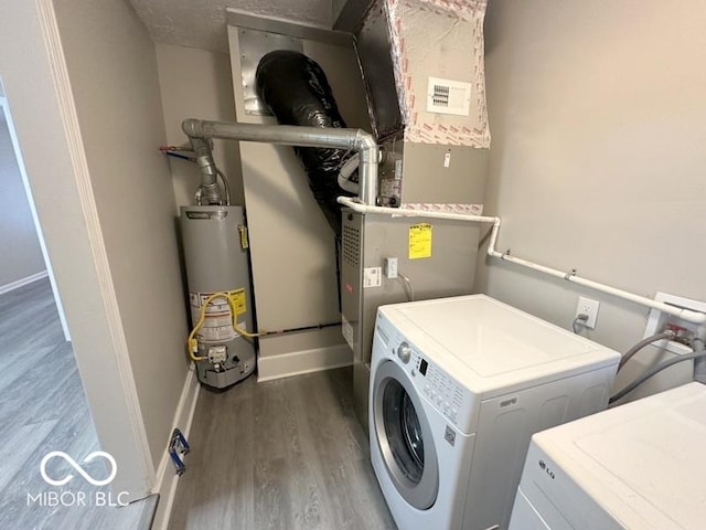 clothes washing area with washing machine and clothes dryer, a textured ceiling, dark hardwood / wood-style floors, and water heater