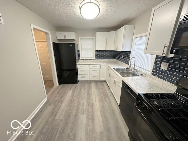 kitchen with backsplash, black appliances, white cabinets, sink, and light wood-type flooring