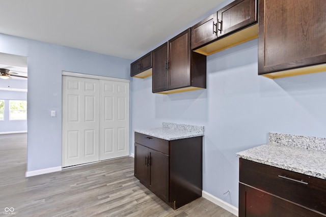 kitchen featuring dark brown cabinets, ceiling fan, light stone counters, and light wood-type flooring