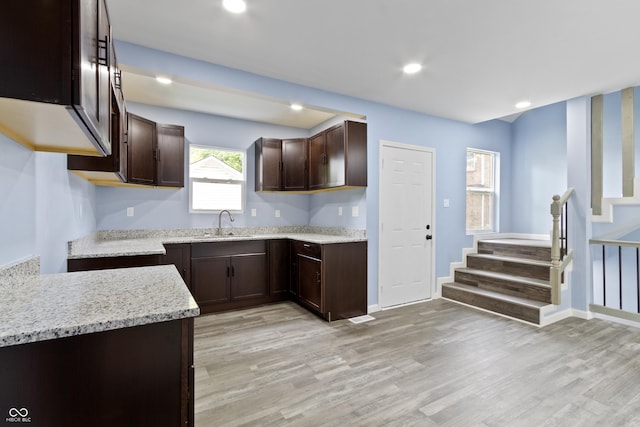 kitchen featuring light stone countertops, dark brown cabinets, light hardwood / wood-style floors, and sink