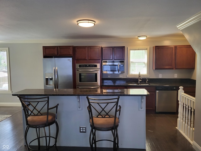 kitchen with a kitchen island, appliances with stainless steel finishes, sink, a kitchen breakfast bar, and ornamental molding