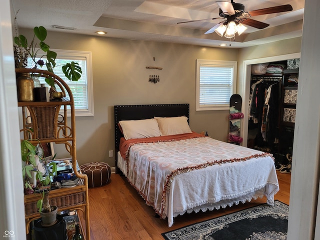 bedroom featuring a raised ceiling, hardwood / wood-style floors, and multiple windows