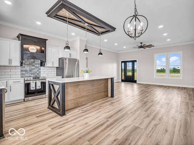 kitchen featuring ceiling fan with notable chandelier, stainless steel appliances, decorative light fixtures, white cabinets, and a center island