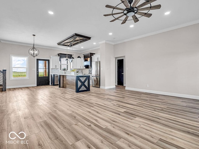 kitchen with stainless steel refrigerator, pendant lighting, a kitchen island, ceiling fan with notable chandelier, and ornamental molding