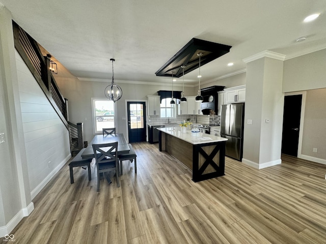 kitchen with decorative backsplash, appliances with stainless steel finishes, a kitchen island, decorative light fixtures, and white cabinetry