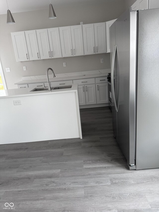 kitchen featuring hanging light fixtures, hardwood / wood-style flooring, white cabinetry, stainless steel fridge, and sink