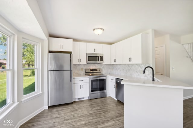 kitchen with stainless steel appliances, white cabinets, kitchen peninsula, hardwood / wood-style floors, and backsplash