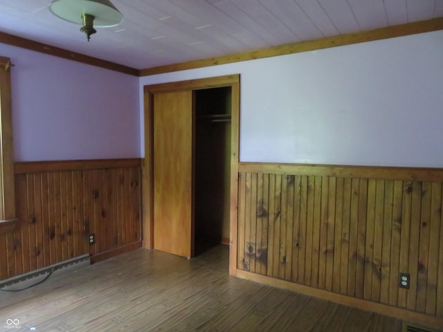 unfurnished bedroom with hardwood / wood-style flooring, baseboard heating, wooden walls, and a closet