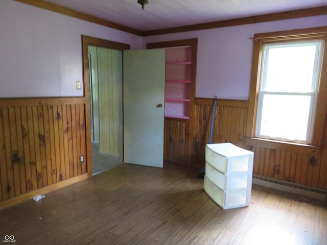 empty room with baseboard heating, wooden walls, hardwood / wood-style floors, and crown molding