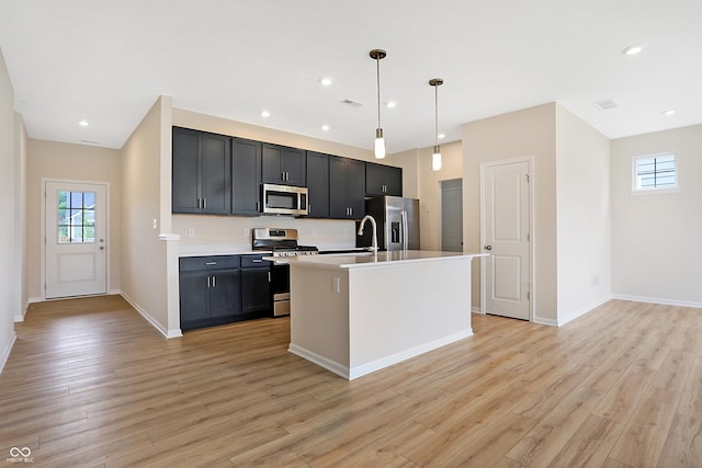 kitchen with sink, stainless steel appliances, decorative light fixtures, a kitchen island with sink, and light wood-type flooring