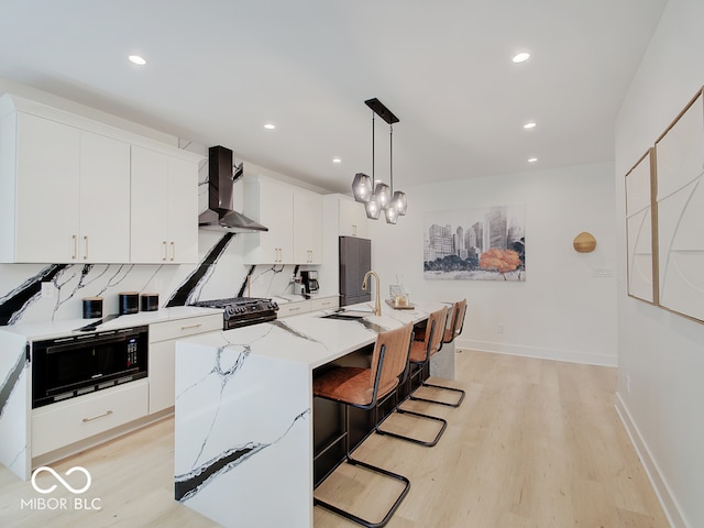 kitchen featuring a center island with sink, wall chimney exhaust hood, black microwave, a sink, and gas stove