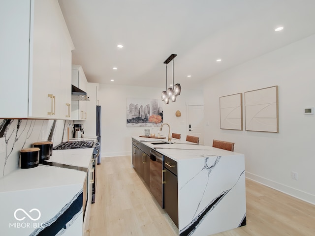 kitchen with an island with sink, light wood-style flooring, under cabinet range hood, white cabinetry, and a sink