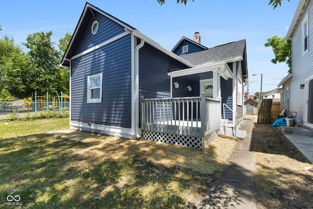 view of front facade with a wooden deck, fence, a chimney, and a front lawn