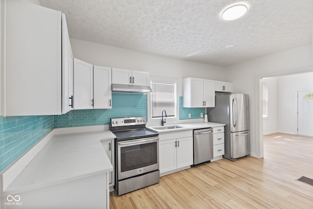 kitchen with white cabinets, appliances with stainless steel finishes, light hardwood / wood-style floors, sink, and a textured ceiling