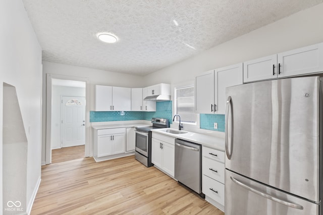 kitchen with under cabinet range hood, a sink, light countertops, appliances with stainless steel finishes, and light wood finished floors