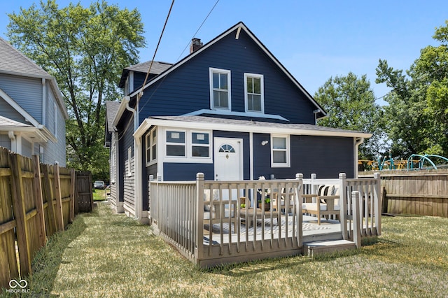 rear view of property with a wooden deck, fence, roof with shingles, and a yard