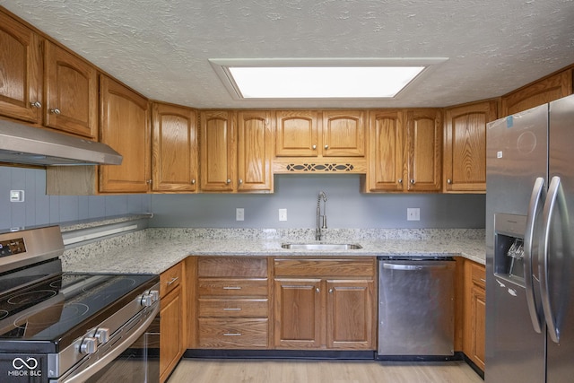 kitchen featuring light stone countertops, a textured ceiling, stainless steel appliances, sink, and light wood-type flooring