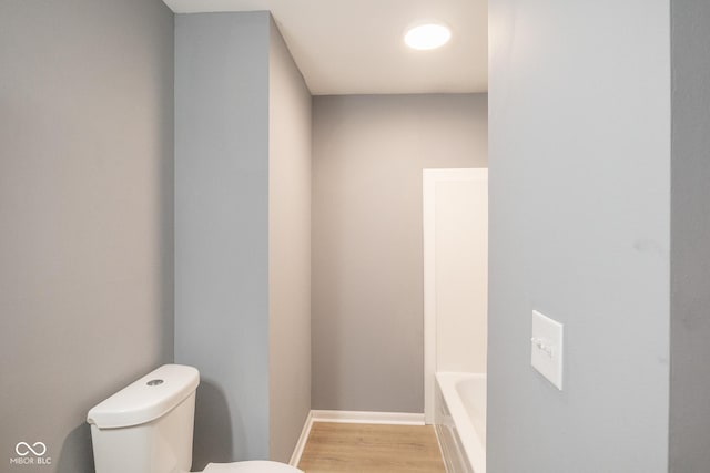 bathroom featuring toilet, hardwood / wood-style floors, and a bath