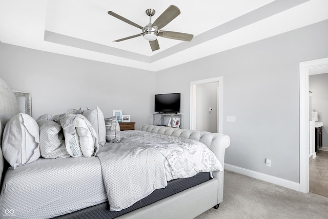 bedroom with a tray ceiling, light colored carpet, connected bathroom, ceiling fan, and baseboards