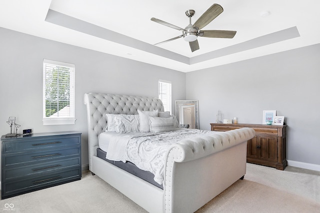 bedroom with light carpet, ceiling fan, a tray ceiling, and baseboards