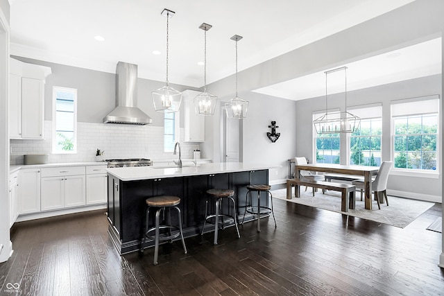 kitchen with a wealth of natural light, light countertops, decorative backsplash, dark wood-type flooring, and wall chimney range hood