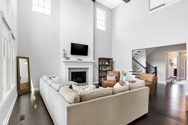 living area featuring dark wood-type flooring, a fireplace, a towering ceiling, visible vents, and stairway