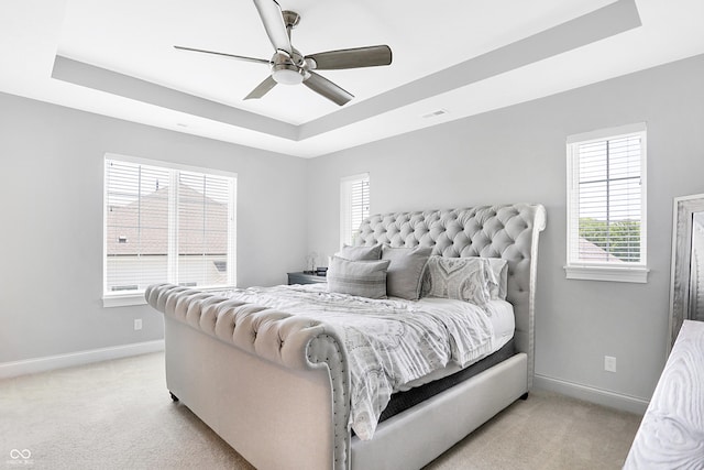 bedroom featuring a tray ceiling, light carpet, visible vents, and baseboards