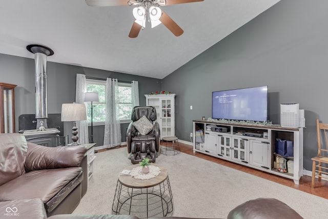 living area with wood finished floors, a ceiling fan, baseboards, vaulted ceiling, and a wood stove