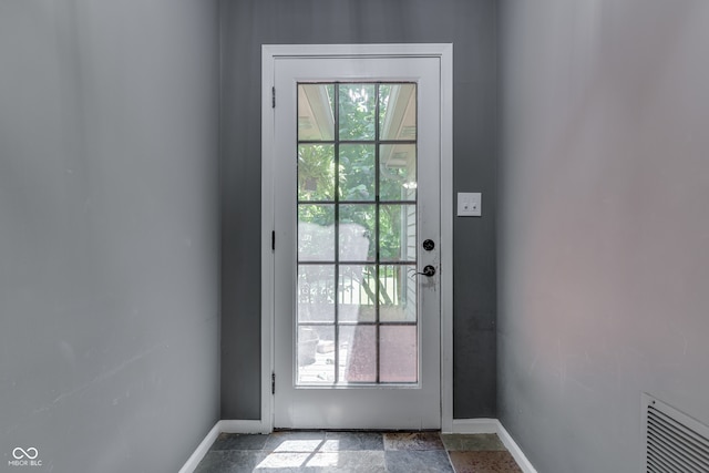 doorway with a wealth of natural light, stone tile flooring, visible vents, and baseboards