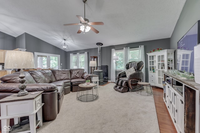 living area featuring lofted ceiling, a wood stove, ceiling fan, a textured ceiling, and wood finished floors