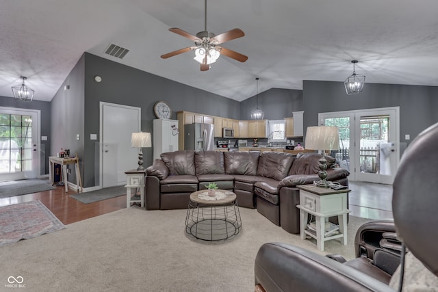 living room featuring visible vents, vaulted ceiling, light carpet, and ceiling fan with notable chandelier