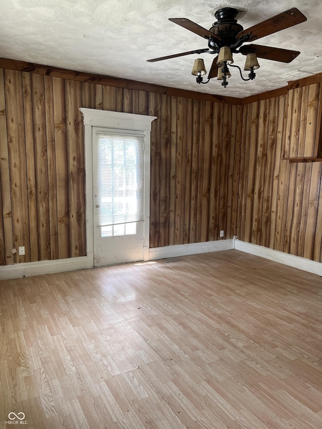 unfurnished room with ceiling fan, wooden walls, light hardwood / wood-style floors, and a textured ceiling