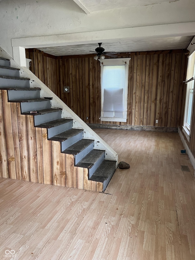 stairway featuring hardwood / wood-style flooring, ceiling fan, and wood walls