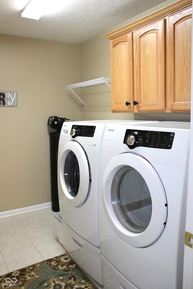 laundry room with cabinets, light tile patterned floors, washing machine and clothes dryer, and a textured ceiling