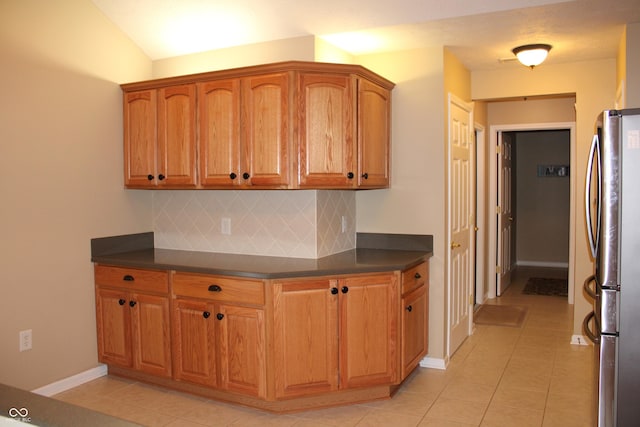 kitchen with stainless steel refrigerator, light tile patterned flooring, and tasteful backsplash