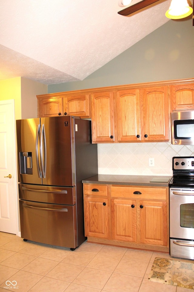 kitchen featuring light tile patterned flooring, lofted ceiling, appliances with stainless steel finishes, and decorative backsplash