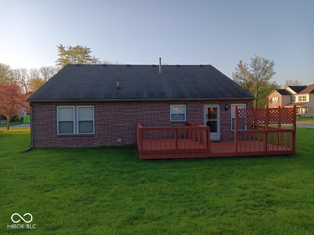 rear view of house featuring a shingled roof, brick siding, a lawn, and a deck