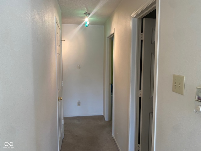 corridor with dark carpet and a textured ceiling