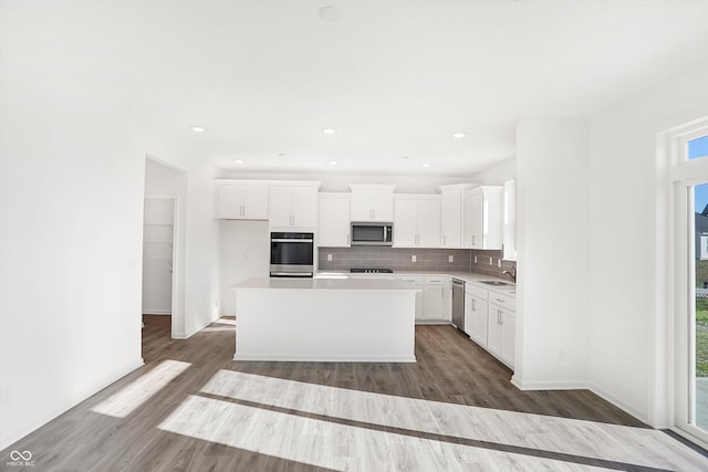 kitchen featuring hardwood / wood-style floors, a center island, decorative backsplash, appliances with stainless steel finishes, and white cabinetry