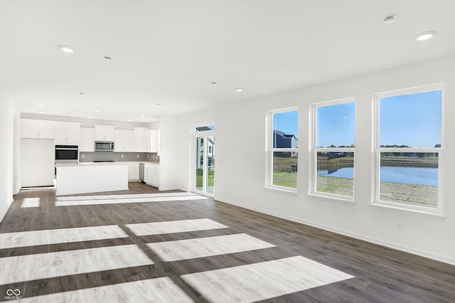 unfurnished living room featuring dark hardwood / wood-style flooring and a water view