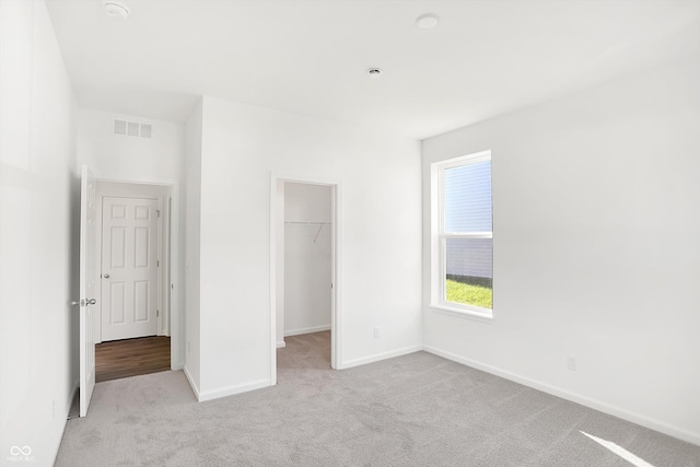 unfurnished bedroom featuring a spacious closet, a closet, and light colored carpet