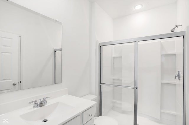 bathroom featuring a shower with door, vanity, and toilet