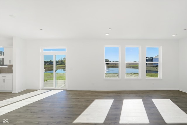 unfurnished living room featuring dark hardwood / wood-style flooring, a water view, and plenty of natural light