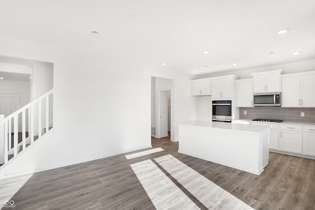 kitchen with hardwood / wood-style floors, backsplash, a kitchen island, white cabinetry, and stainless steel appliances