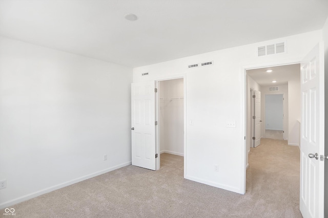 unfurnished bedroom featuring a walk in closet, light colored carpet, and a closet