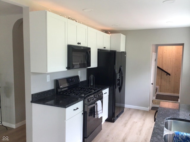 kitchen with sink, white cabinetry, dark stone countertops, gas stove, and light wood-type flooring